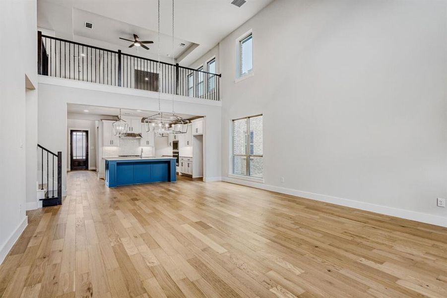 Unfurnished living room with a ceiling fan, light wood-style flooring, suspended lighting, and a high ceiling