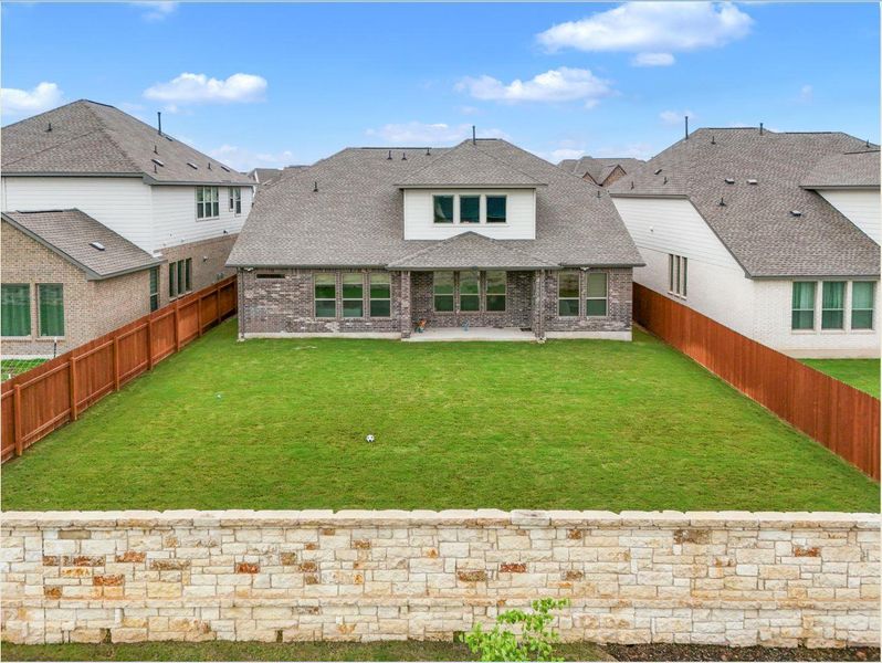 A spacious, verdant yard with ample room for outdoor activities, bordered by a stone retaining wall and privacy fencing.