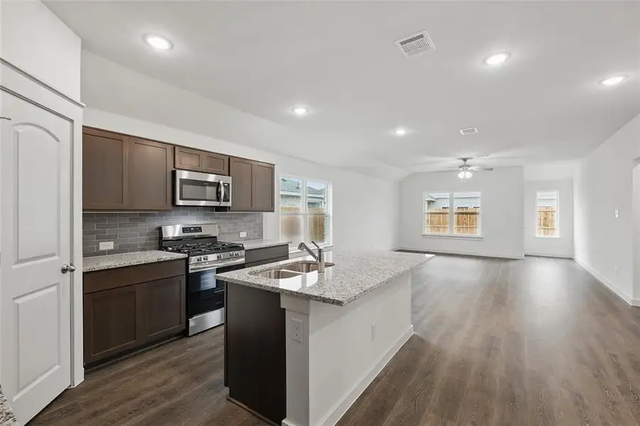 Kitchen with stainless steel appliances, light stone counters, a center island with sink, dark wood-style flooring, and tasteful backsplash Kitchen with stainless steel appliances, light stone counters, a center island with sink, dark wood-style flooring, and tasteful backsplash