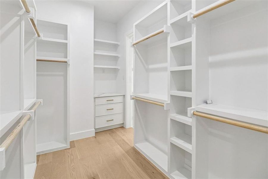 Custom closet system featuring light wood-finish flooring, white built-in shelving, hanging rods, and a three-drawer built-in cabinet with gold-tone hardware and a stone-finish countertop