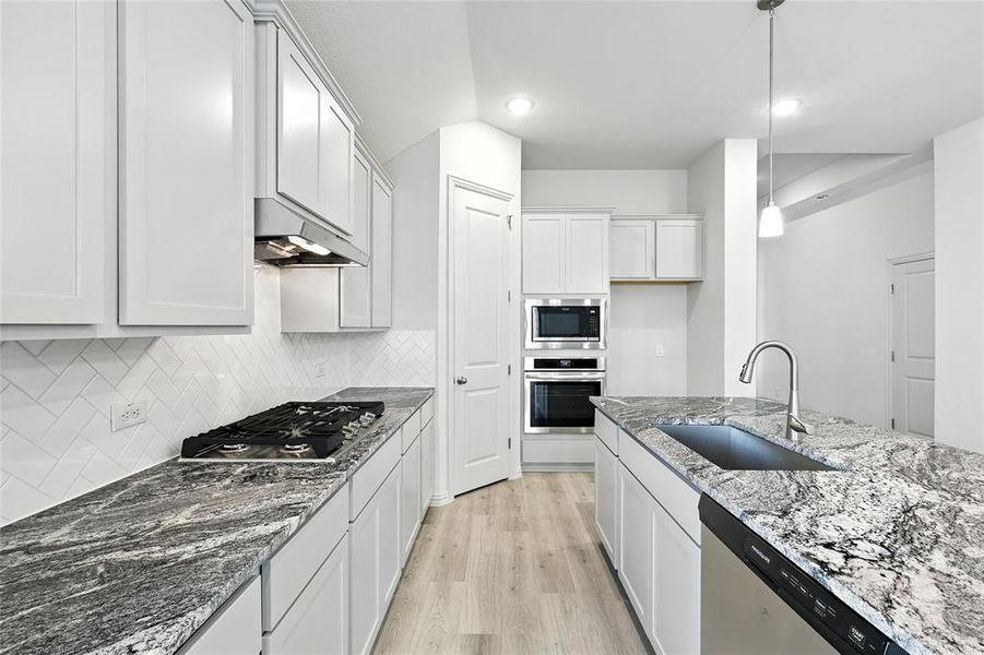 Kitchen with stainless steel appliances, under cabinet range hood, decorative backsplash, light wood-type flooring, and stone counters Kitchen with stainless steel appliances, under cabinet range hood, decorative backsplash, light wood-type flooring, and stone counters