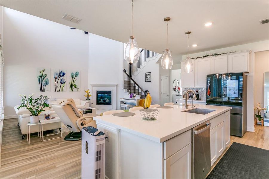 Kitchen featuring white cabinets, decorative light fixtures, light wood finished floors, appliances with stainless steel finishes, and open floor plan