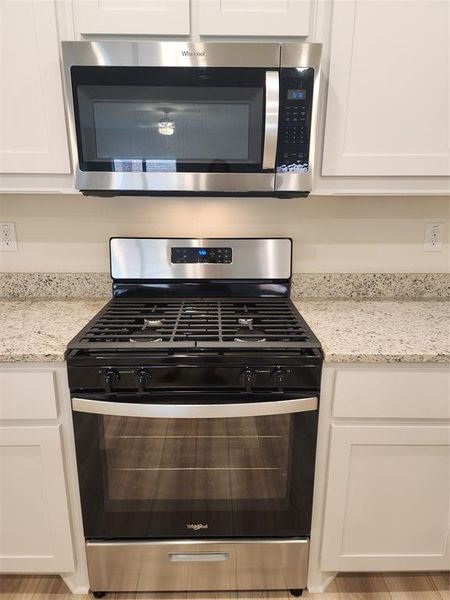 Kitchen view of gas range, light stone counters, and white cabinetry Kitchen view of gas range, light stone counters, and white cabinetry