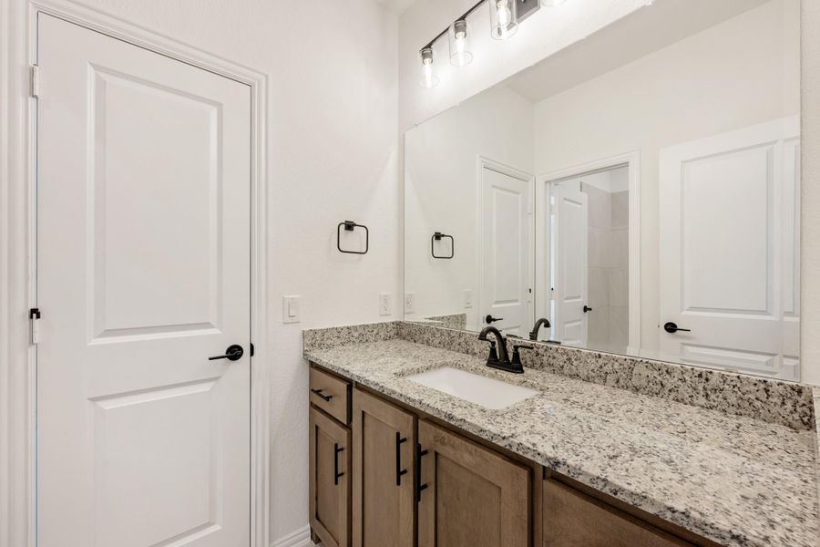 Bathroom vanity with granite countertop, wood cabinets, single sink, and large mirror with overhead lighting