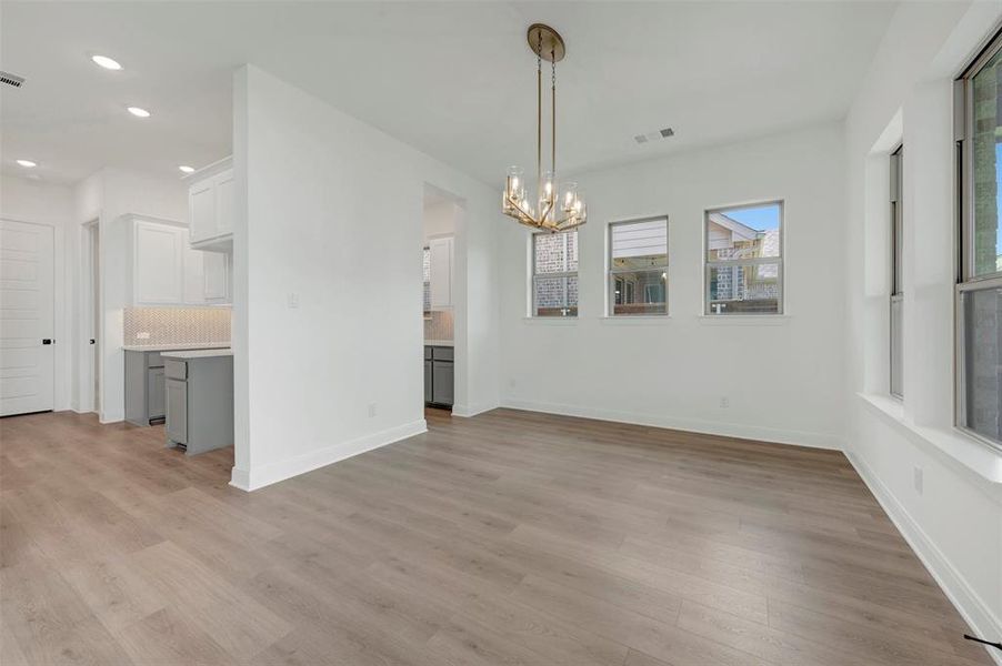 Open-concept living space featuring wood-finish flooring, a modern chandelier, multiple windows, recessed lighting, and a partial view of the kitchen with light cabinetry Open-concept living space featuring wood-finish flooring, a modern chandelier, multiple windows, recessed lighting, and a partial view of the kitchen with light cabinetry