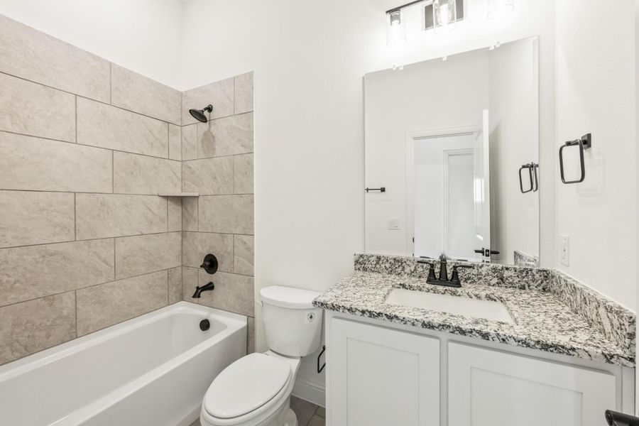 Bathroom with tiled tub-shower combo, white vanity with granite countertop, and black fixtures
