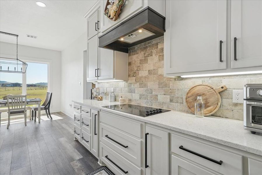 Kitchen featuring light stone counters, custom range hood, white cabinetry, dark wood-type flooring, and recessed lighting