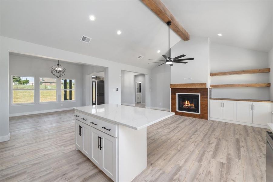Kitchen featuring light stone counters, light wood-style floors, a center island, a glass covered fireplace, and white cabinetry