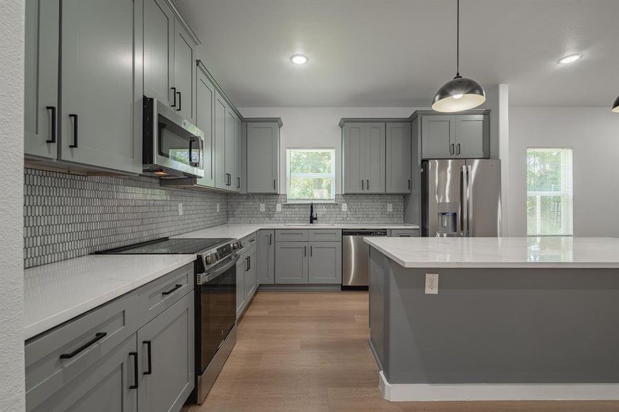 Kitchen featuring appliances with stainless steel finishes, gray cabinetry, backsplash, light wood finished floors, and recessed lighting Kitchen featuring appliances with stainless steel finishes, gray cabinetry, backsplash, light wood finished floors, and recessed lighting