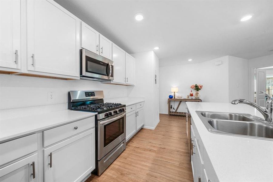 his view showcases a modern kitchen with stainless steel appliances, white cabinets, and quartz countertops, offering a clean and functional design.