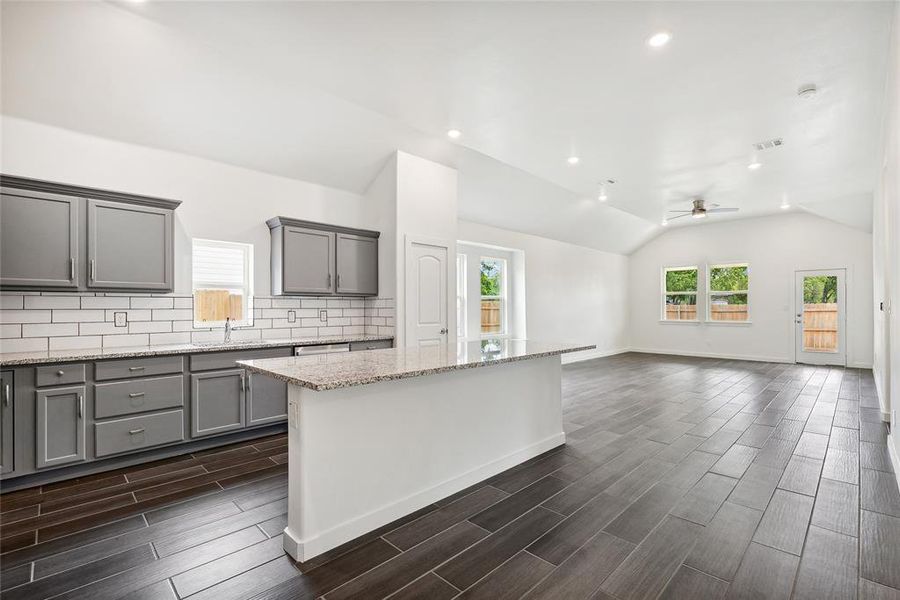 Kitchen featuring tasteful backsplash, dark hardwood / wood-style flooring, light stone countertops, ceiling fan, and vaulted ceiling