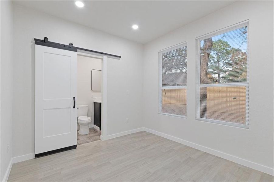 Unfurnished bedroom featuring a barn door, ensuite bathroom, and light wood-type flooring