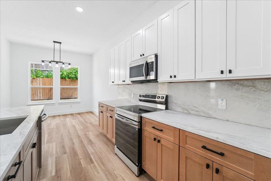 Kitchen featuring white upper cabinetry, natural wood-finish lower cabinetry, stone countertops, stainless steel appliances, and wood-finish flooring Kitchen featuring white upper cabinetry, natural wood-finish lower cabinetry, stone countertops, stainless steel appliances, and wood-finish flooring