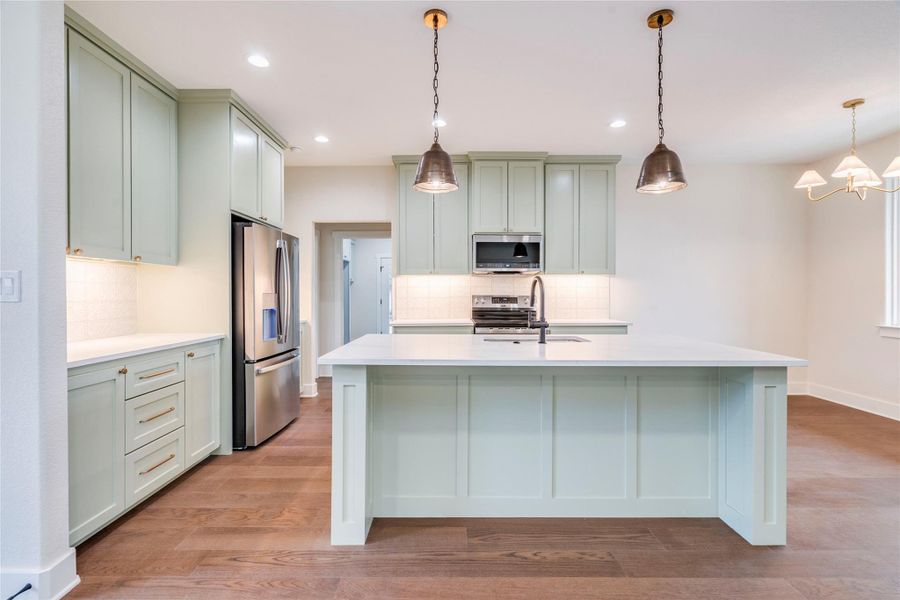 Kitchen with decorative light fixtures, stainless steel appliances, a center island with sink, light wood-type flooring, and recessed lighting