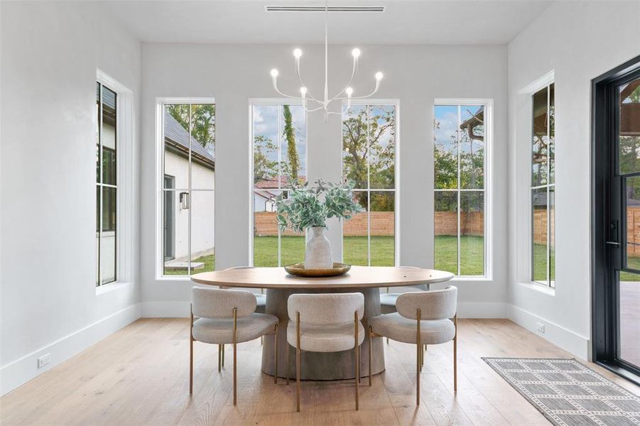 This is a bright, modern breakfast room complemented by a chic chandelier. Large windows let in ample natural light, and the space is accentuated by neutral colors. Your view looks out these picturesque wood-framed windows into your private backyard.