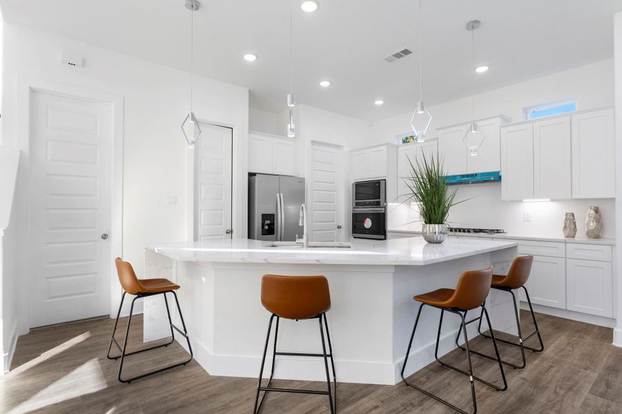 Modern kitchen featuring a spacious island, quartz countertops, built-in appliances, and stylish pendant lighting.