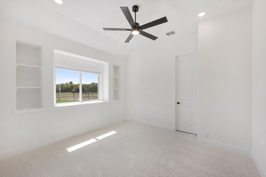 Empty bedroom with vaulted ceiling, ceiling fan, built-in shelves, and carpet flooring
