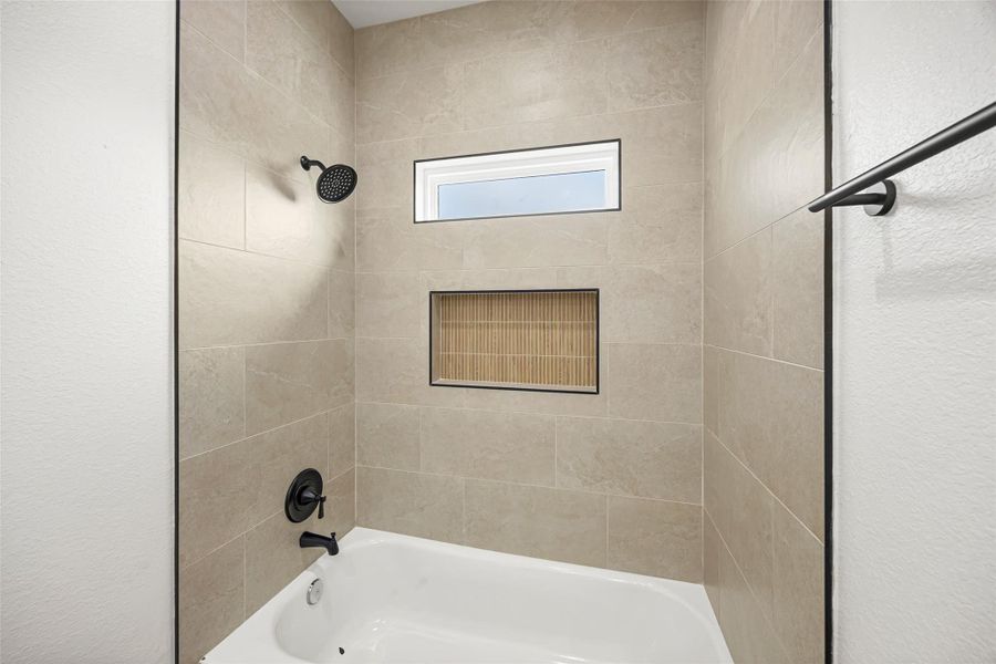 Modern tiled tub/shower with built-in niche and black hardware accents.