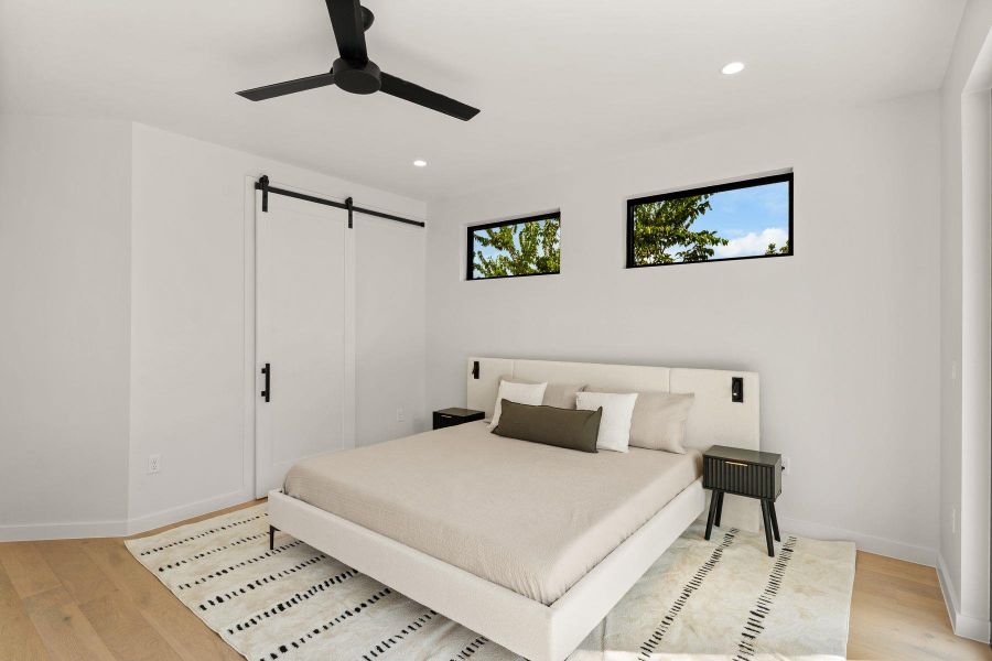 High windows invite natural light and leafy views into this modern bedroom with wood floors.