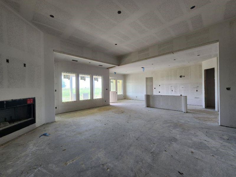 Open-concept interior featuring a built-in fireplace, multiple large windows, and a partially framed island structure