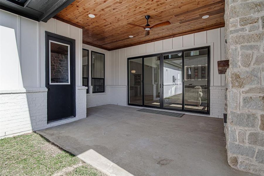 Entrance to property with a patio, a ceiling fan, and board and batten siding. Slide and stack patio doors. Entrance to property with a patio, a ceiling fan, and board and batten siding. Slide and stack patio doors.