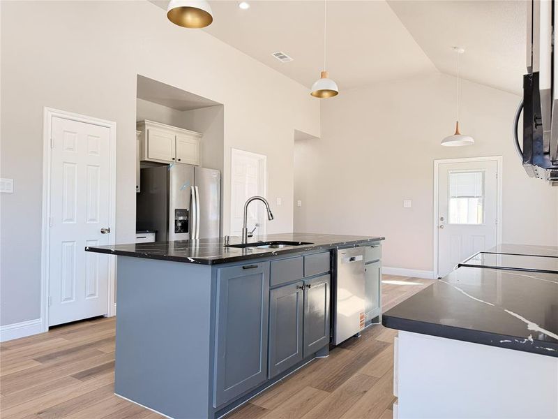Kitchen with a center island with sink, light wood finished floors, stainless steel appliances, decorative light fixtures, and lofted ceiling
