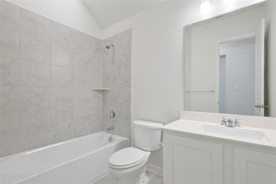 Bathroom featuring vanity, shower / bathtub combination, a textured wall, and vaulted ceiling