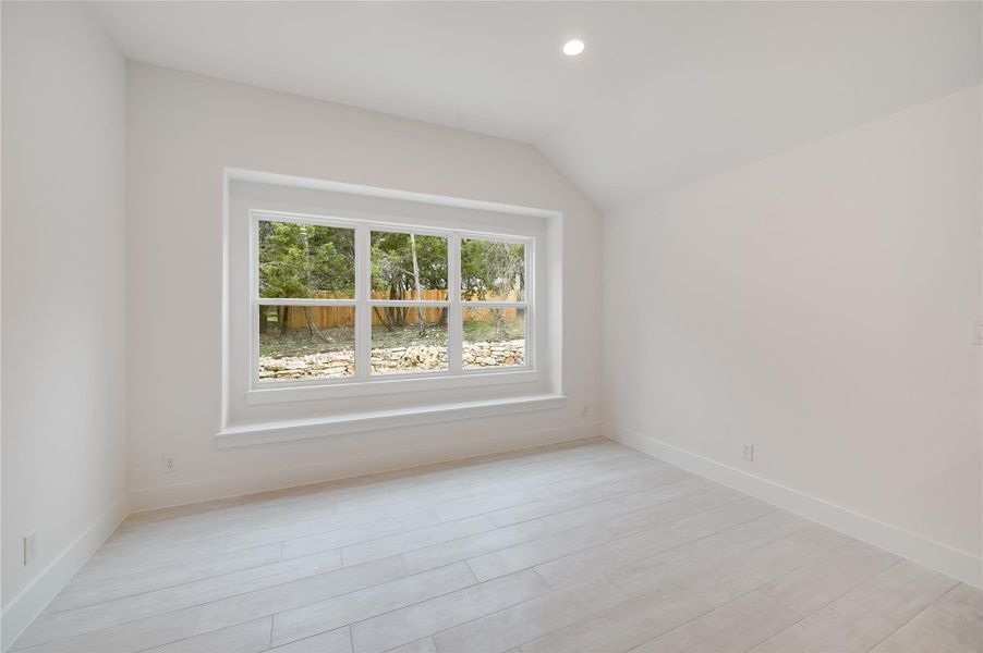 Spare room featuring light wood-style floors, baseboards, vaulted ceiling, and recessed lighting