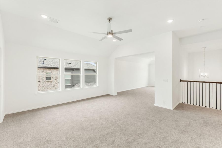 Open upstairs bonus room with vaulted ceiling, ceiling fan, carpet, and staircase railing