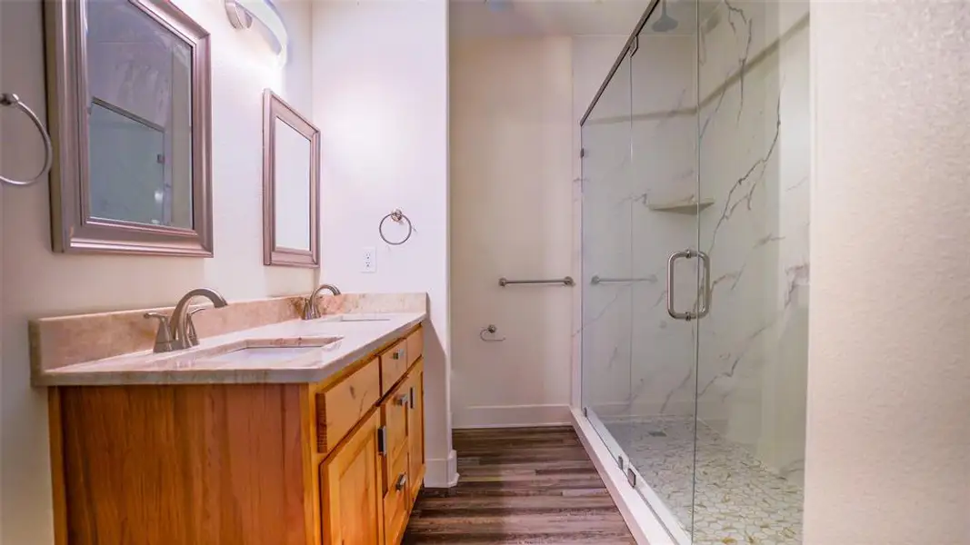 Primary bath with double vanity, a marble finish shower, and wood-style floors Primary bath with double vanity, a marble finish shower, and wood-style floors