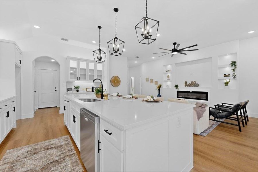 Kitchen with glass fronted cabinets, white cabinets, ceiling fan, a large island, and light stone counters Kitchen with glass fronted cabinets, white cabinets, ceiling fan, a large island, and light stone counters