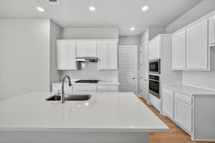 Kitchen with light stone countertops, white cabinetry, recessed lighting, backsplash, and a kitchen island with sink Kitchen with light stone countertops, white cabinetry, recessed lighting, backsplash, and a kitchen island with sink