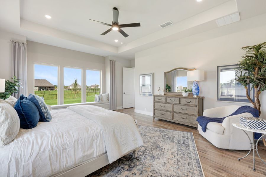 Master bedroom with hardwood floors, ceiling fan, large windows, and wood dresser with mirror