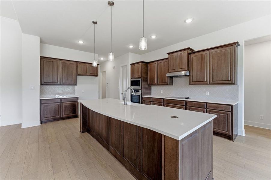 Spacious kitchen featuring a large curved island with a white countertop and three pendant lights Spacious kitchen featuring a large curved island with a white countertop and three pendant lights