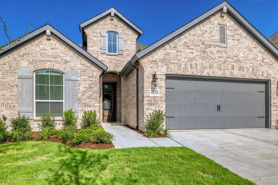 Brick exterior with a prominent arched entry, attached garage with decorative hardware, and architectural rooflines