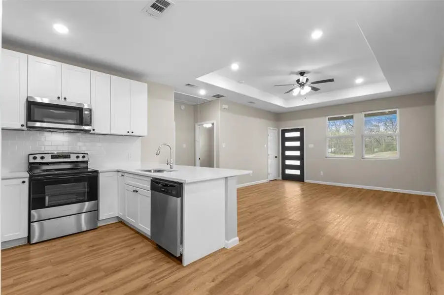 Kitchen with appliances with stainless steel finishes, white cabinetry, a peninsula, backsplash, and open floor plan
