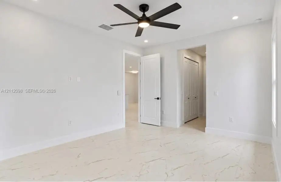 Interior space featuring large-format veined tile flooring, matte black ceiling fan with integrated lighting, recessed lighting, and solid-core panel doors Interior space featuring large-format veined tile flooring, matte black ceiling fan with integrated lighting, recessed lighting, and solid-core panel doors