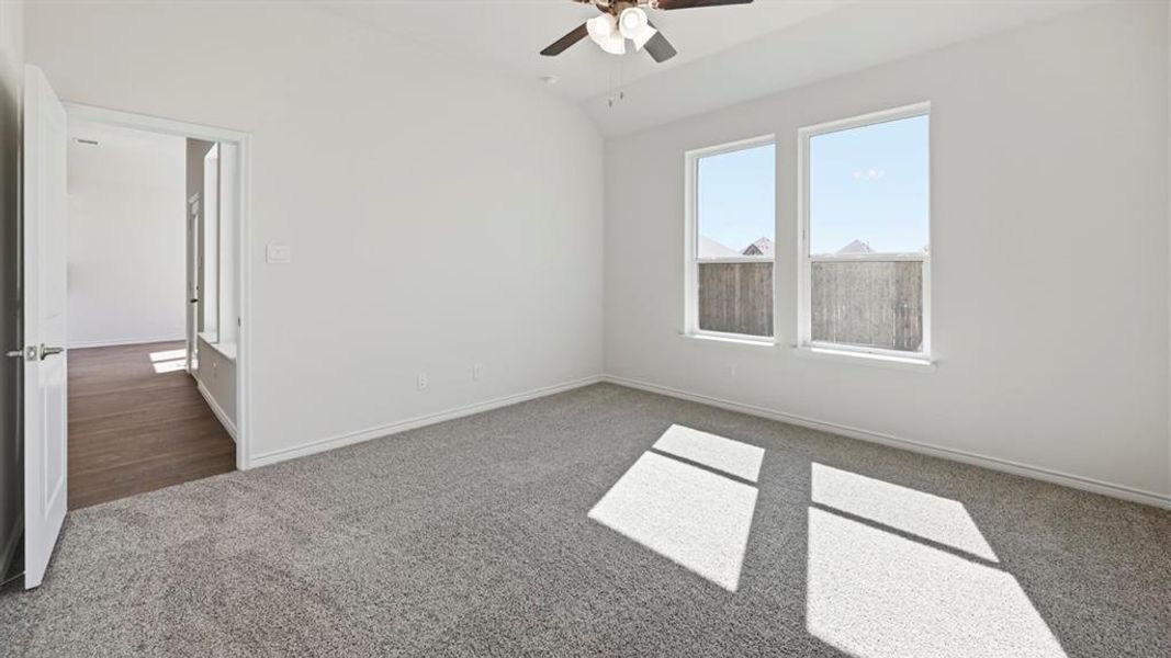 Carpeted interior space featuring a ceiling fan with integrated lighting, a white painted door with brushed nickel hardware, and two large windows Carpeted interior space featuring a ceiling fan with integrated lighting, a white painted door with brushed nickel hardware, and two large windows