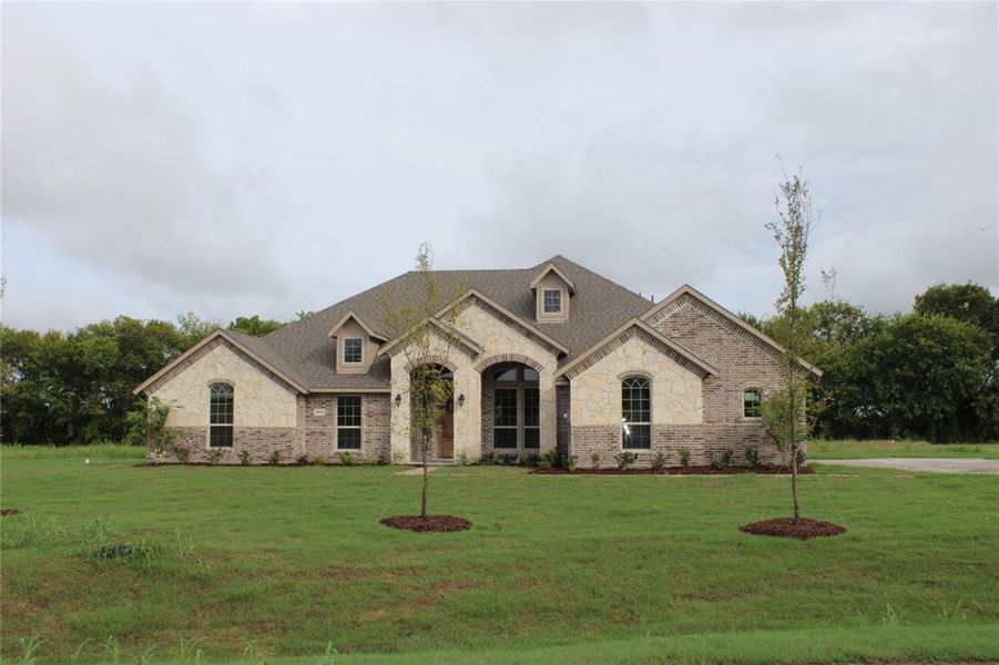 French country home with stone siding, a front yard, and brick siding French country home with stone siding, a front yard, and brick siding