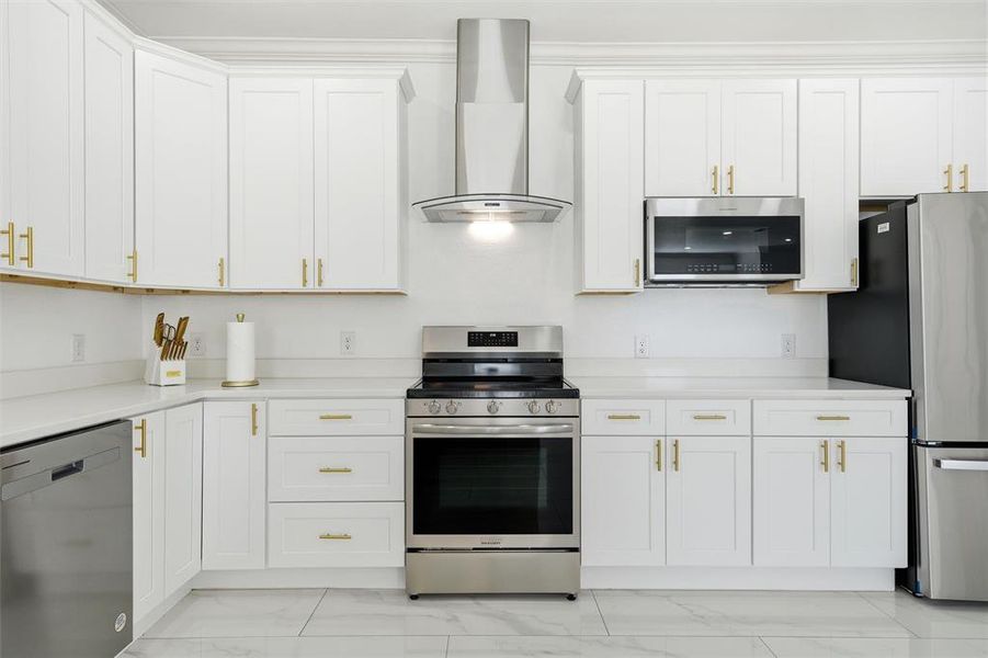 Kitchen featuring stainless steel appliances, wall chimney range hood, light marble finish floors, and white cabinetry Kitchen featuring stainless steel appliances, wall chimney range hood, light marble finish floors, and white cabinetry