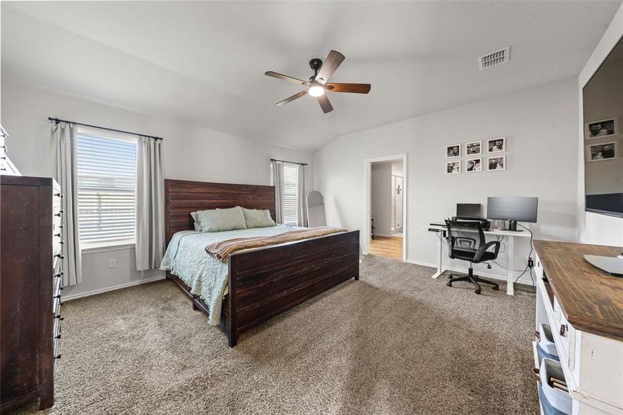 Carpeted bedroom with multiple windows, vaulted ceiling, a desk, and ceiling fan
