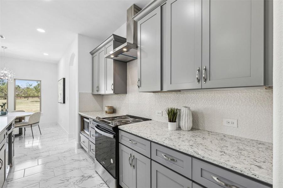 Kitchen with light stone countertops, light tile patterned flooring, gray cabinetry, range, and wall chimney exhaust hood