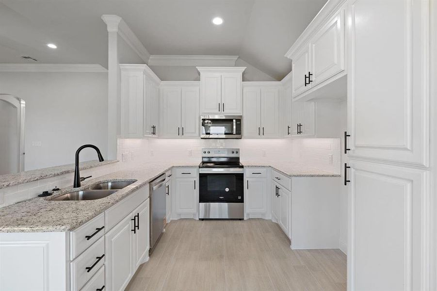 Kitchen with stainless steel appliances, decorative backsplash, white cabinets, light stone countertops, and ornamental molding
