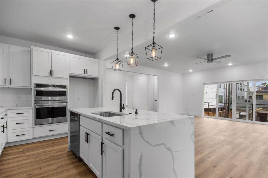 Kitchen featuring hardwood / wood-style floors, an island with sink, white cabinetry, sink, and light stone counters