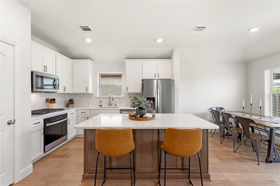 Kitchen featuring a wood-finish island with a light-toned countertop, stainless steel appliances, white cabinetry with dark hardware, and light wood-finish flooring