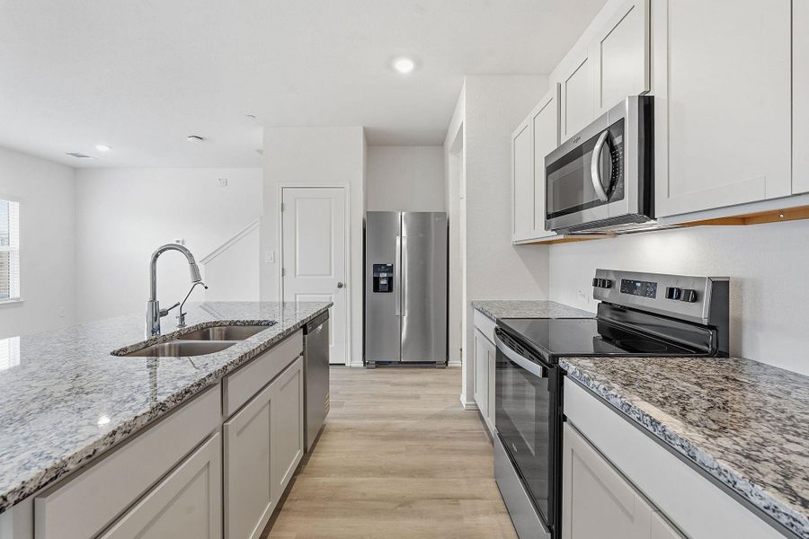 Kitchen featuring granite countertops, stainless steel appliances, light wood-finish flooring, white cabinetry, and a double basin sink with a high-arc faucet Kitchen featuring granite countertops, stainless steel appliances, light wood-finish flooring, white cabinetry, and a double basin sink with a high-arc faucet