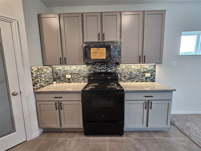 Kitchen featuring light stone counters, gray cabinets, light tile patterned floors, tasteful backsplash, and black electric range