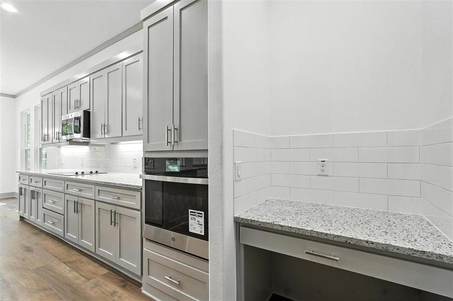 Kitchen featuring gray cabinets, tasteful backsplash, stainless steel appliances, light stone counters, and dark wood-style flooring Kitchen featuring gray cabinets, tasteful backsplash, stainless steel appliances, light stone counters, and dark wood-style flooring