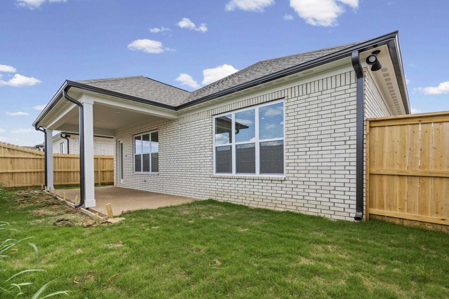 Rear exterior featuring a covered patio with concrete flooring, white brick siding, a dark shingle roof, and black rain gutters Rear exterior featuring a covered patio with concrete flooring, white brick siding, a dark shingle roof, and black rain gutters