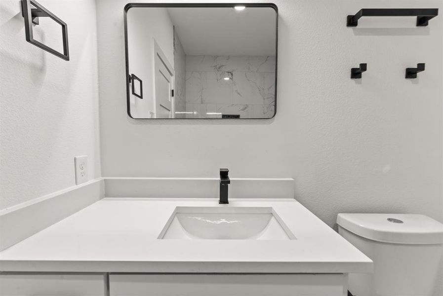 Guest bathroom featuring toilet, a textured wall, and vanity